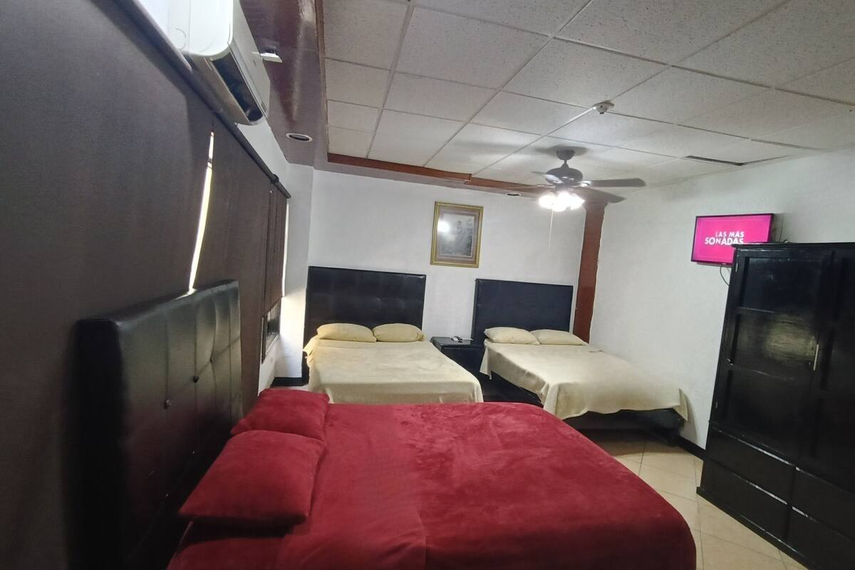 Ein Hotelzimmer mit zwei Betten, einem Deckenventilator, einem Fernseher und einem Kleiderschrank.