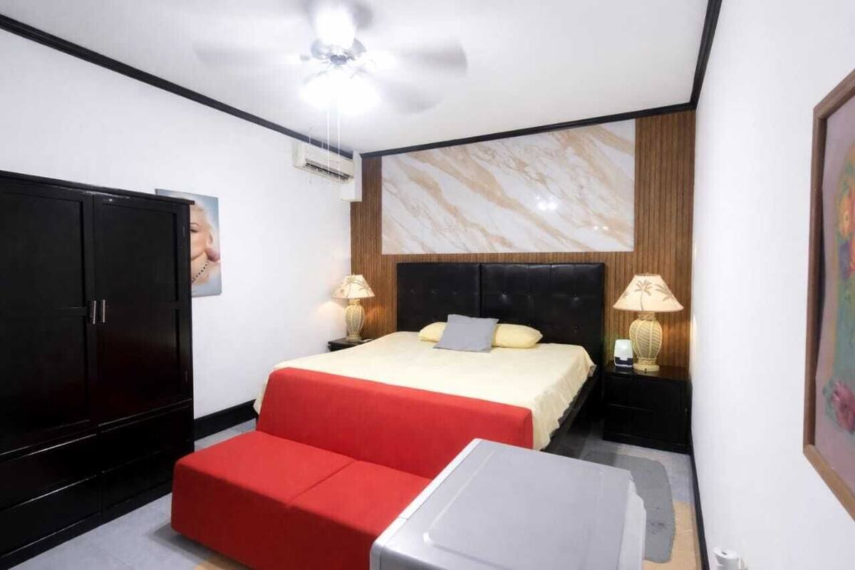 Ein Hotelzimmer mit einem Bett, zwei Nachttischlampen, einem roten Sofa, einem kleinen Tisch und einem Kleiderschrank.