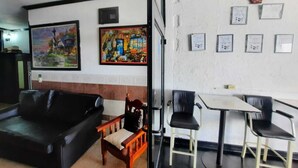 A living room with a black sofa, a wooden chair, and a dining table with four chairs. There are framed pictures on the wall. - Hotel Garcias Suites (Linares)