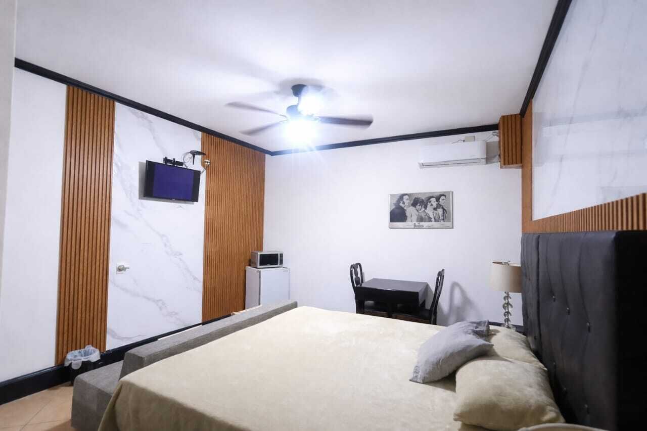 Une chambre à coucher comprenant un lit, un bureau, une chaise, un ventilateur de plafond et un téléviseur.