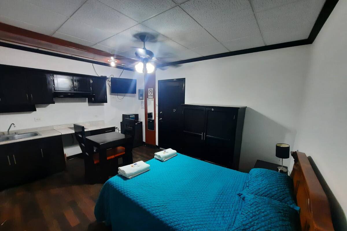 Ein kleines Hotelzimmer mit einem Bett, einem Schreibtisch, einem Stuhl, einer Küchenzeile und einem Kleiderschrank.
