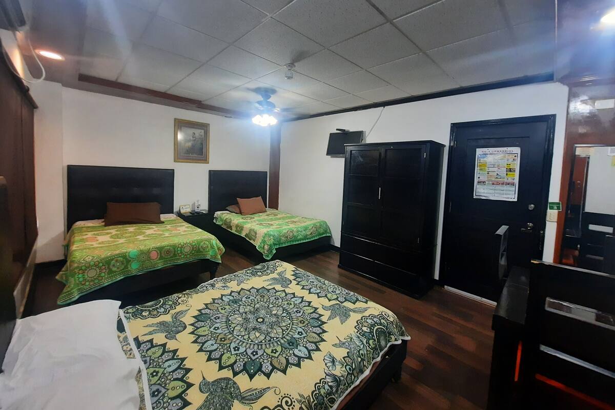 Ein Hotelzimmer mit zwei Einzelbetten, einem großen Kleiderschrank, einem Schreibtisch und einem Deckenventilator.
