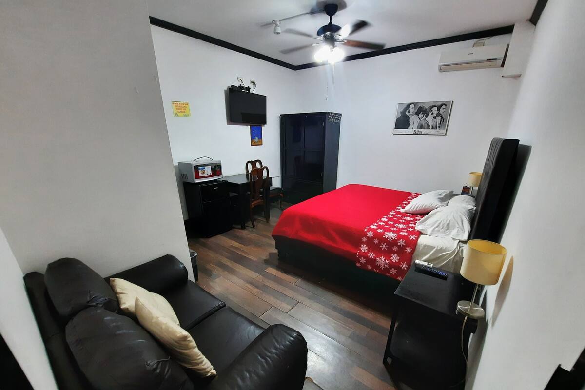 Ein Schlafzimmer mit einem Bett, einem Schreibtisch, einem Stuhl, einem Fernseher und einem Deckenventilator.