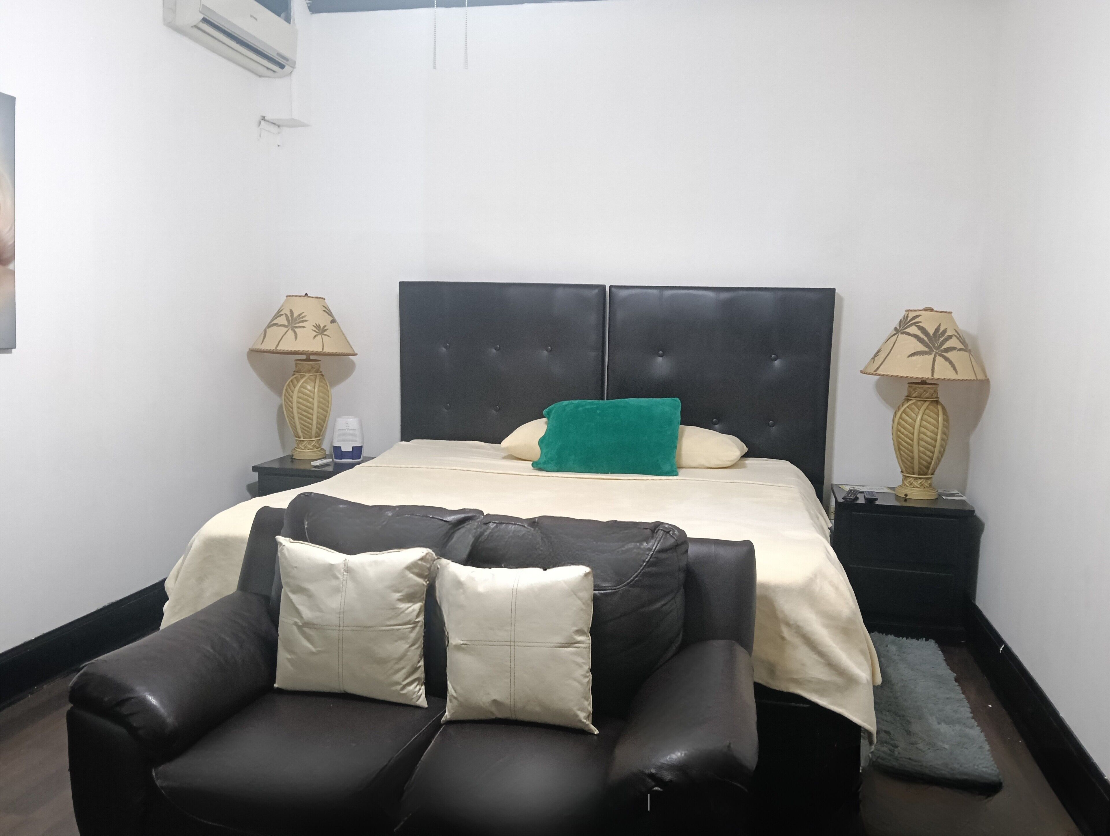 Ein Schlafzimmer mit einem Bett, zwei Nachttischen, einem Sofa und einer Wandklimaanlage.