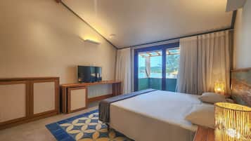 Habitación de hotel con cama, televisor, escritorio con lámpara y vista al mar a través de la ventana.