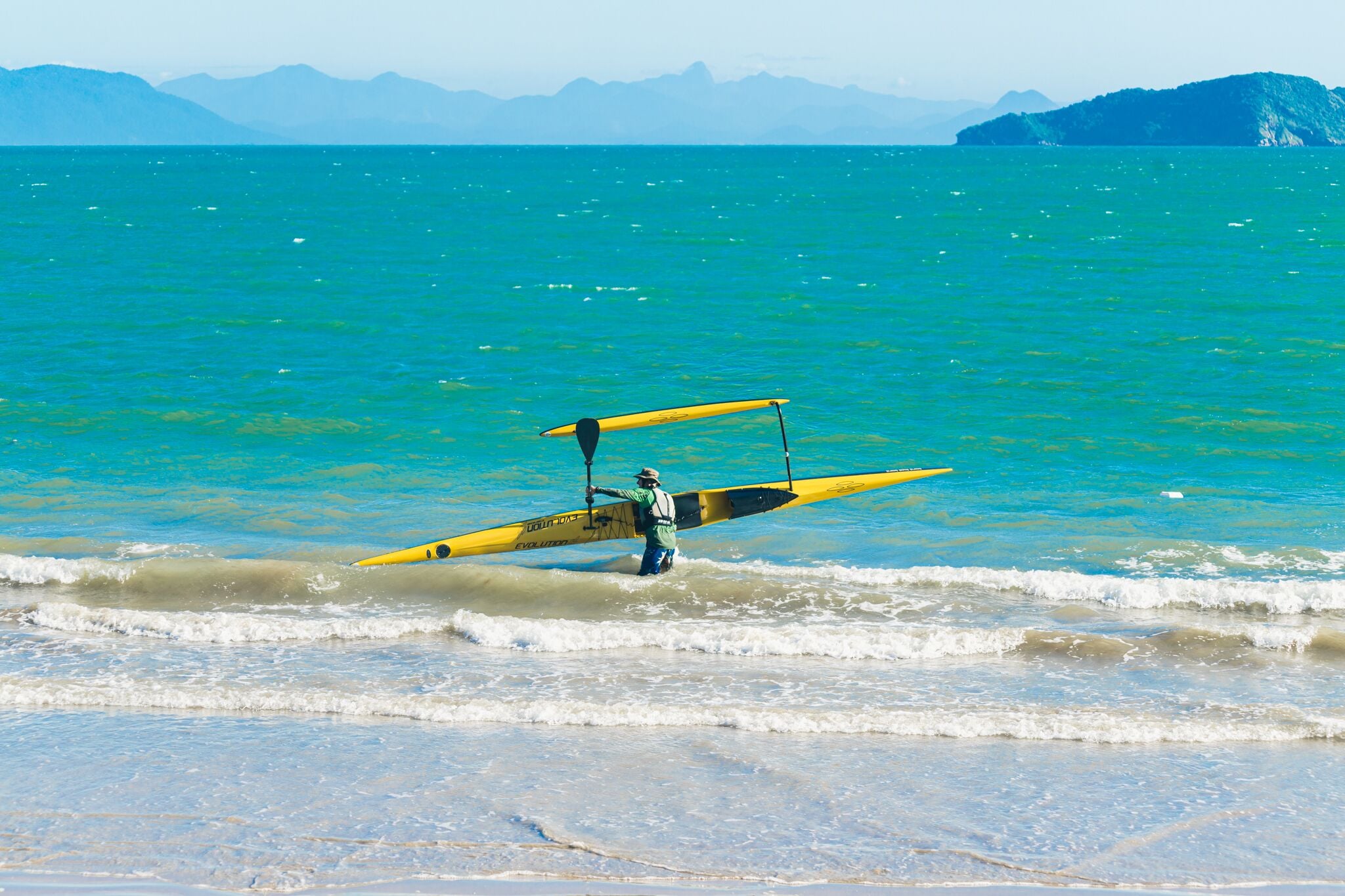 A beach scene with a kayak and a person standing in shallow water.