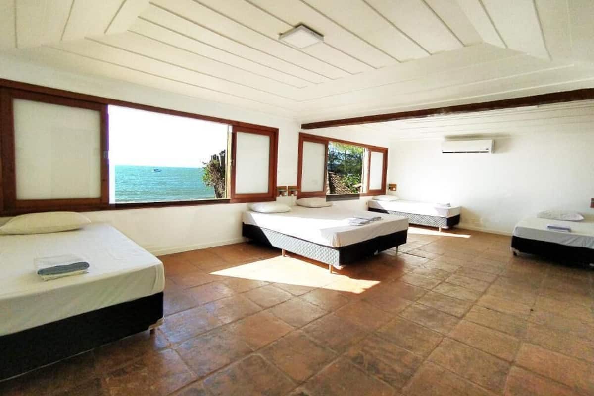 Ein Zimmer mit zwei Betten, einem großen Fenster mit Meerblick und einem Deckenventilator.