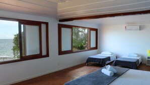 Una habitación con dos camas, una ventana con vistas al mar y un equipo de aire acondicionado en la pared.