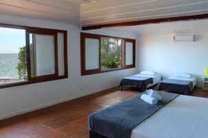 Um quarto com duas camas, uma janela com vista para o mar e um ar condicionado na parede.