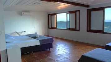 Eine kleine, einfache Unterkunft mit einem Bett, einem kleinen Tisch und Meerblick durch große Fenster.