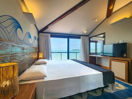 Quarto de hotel com uma cama grande, televisão e vista para o mar.