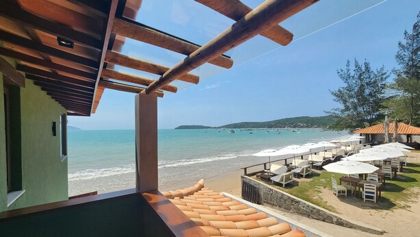 Un balcón con vista a la playa, mobiliario exterior y sombrillas.