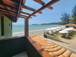 Varanda com vista para a praia, mobiliário de exterior e guarda-sóis.