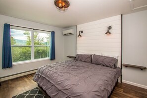 A bedroom with a large bed, a window with curtains, an air conditioning unit, and a wall-mounted shelf.