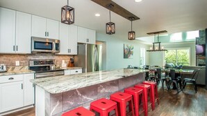 Une cuisine moderne avec des meubles blancs, un îlot en marbre agrémenté de tabourets de bar rouges, et un coin repas avec une table en verre et des chaises noires.
