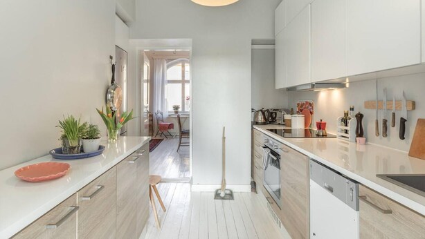 A modern kitchen with white cabinets, a central island, and a dining area visible through an archway. - Cosy Quiet Apartment Close to the Sea and Parks (Helsinki)