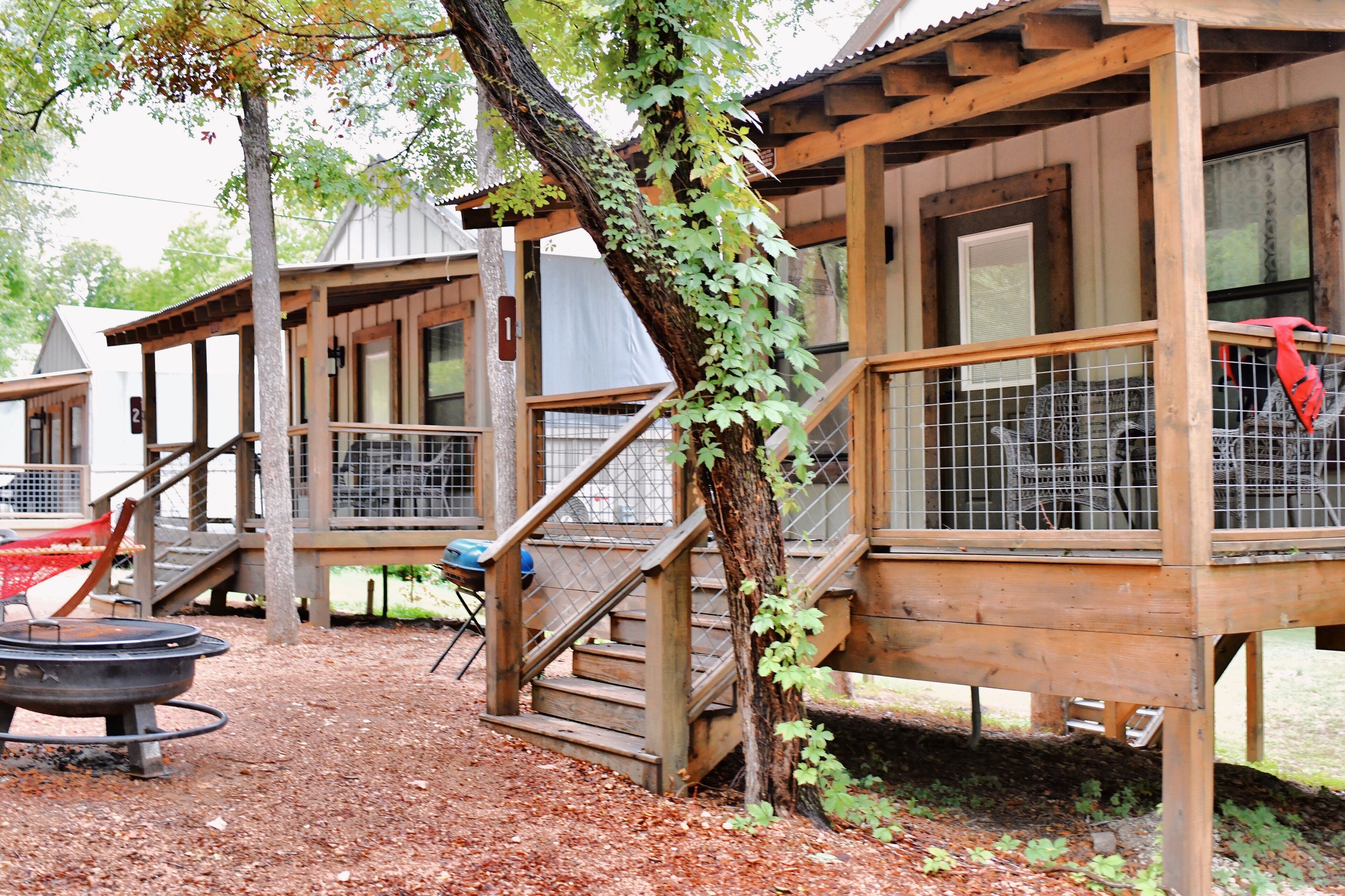 A rustic wooden building with a covered outdoor area, a fire pit, and a fenced enclosure.
