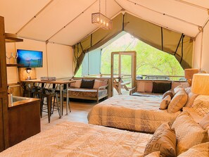 Un alloggio in tenda con zona pranzo, TV e letto con biancheria decorata.