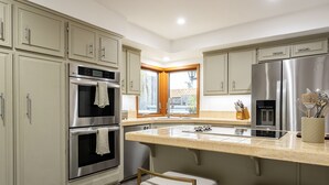 Una cocina moderna con electrodomésticos de acero inoxidable, una isla grande con taburetes de bar y vistas a través de una ventana.
