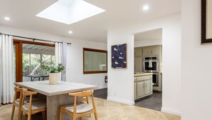 Una cocina moderna con armarios blancos, un horno de acero inoxidable y una zona de comedor con mesa y sillas de madera.