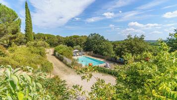 Un jardin à l’arrière de la maison, avec une piscine, entouré d’une végétation luxuriante et d’un grand arbre.