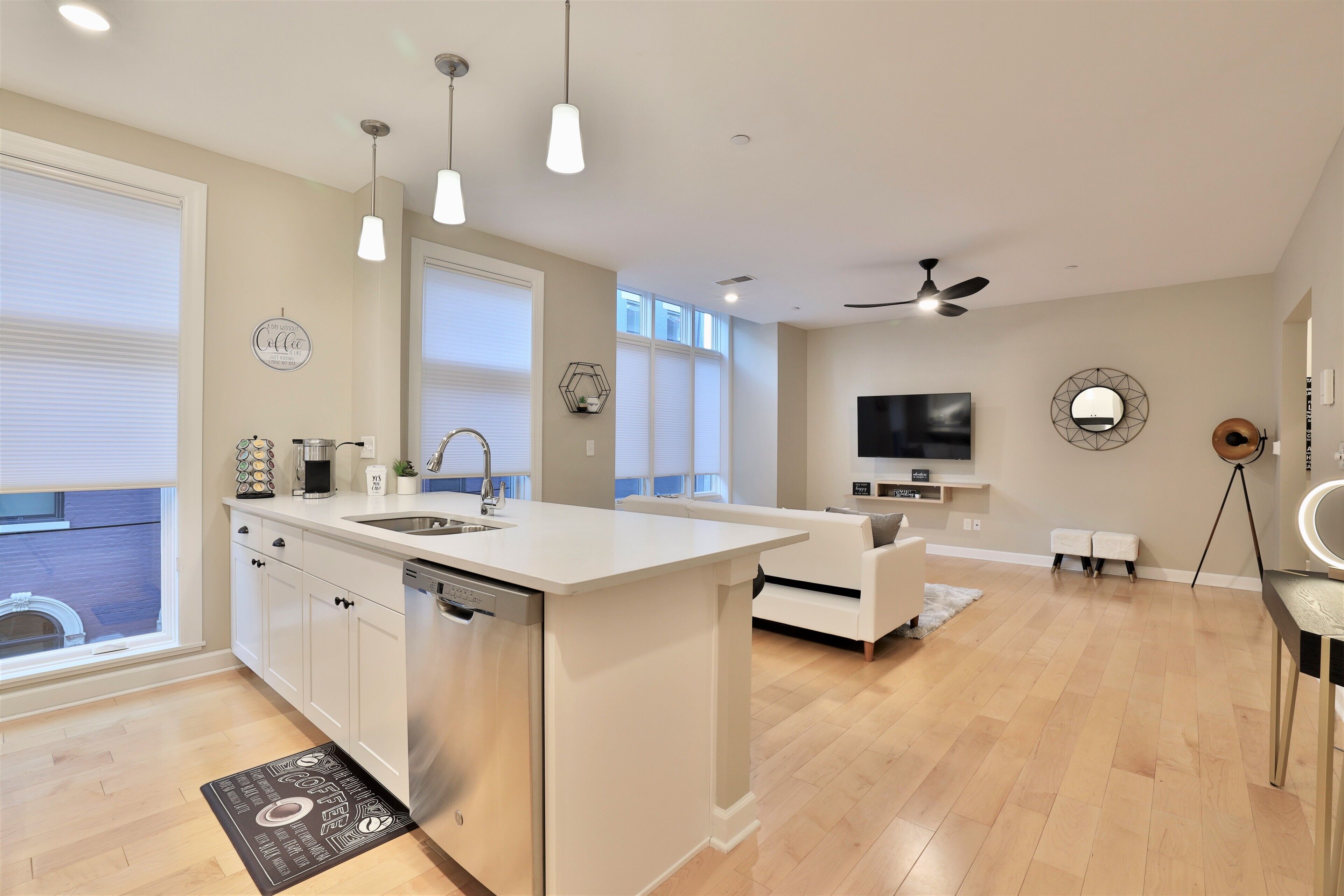 A modern kitchen with a central island, a dining area with a white sofa, and a TV mounted on the wall.