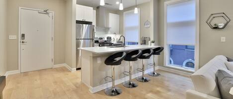 A modern kitchen with a central island, bar stools, pendant lighting, and a large window with a view.
