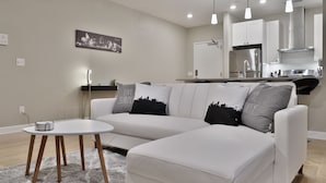 Un salon moderne avec un canapé blanc, une table basse ronde et un tableau représentant un paysage urbain accroché au mur.