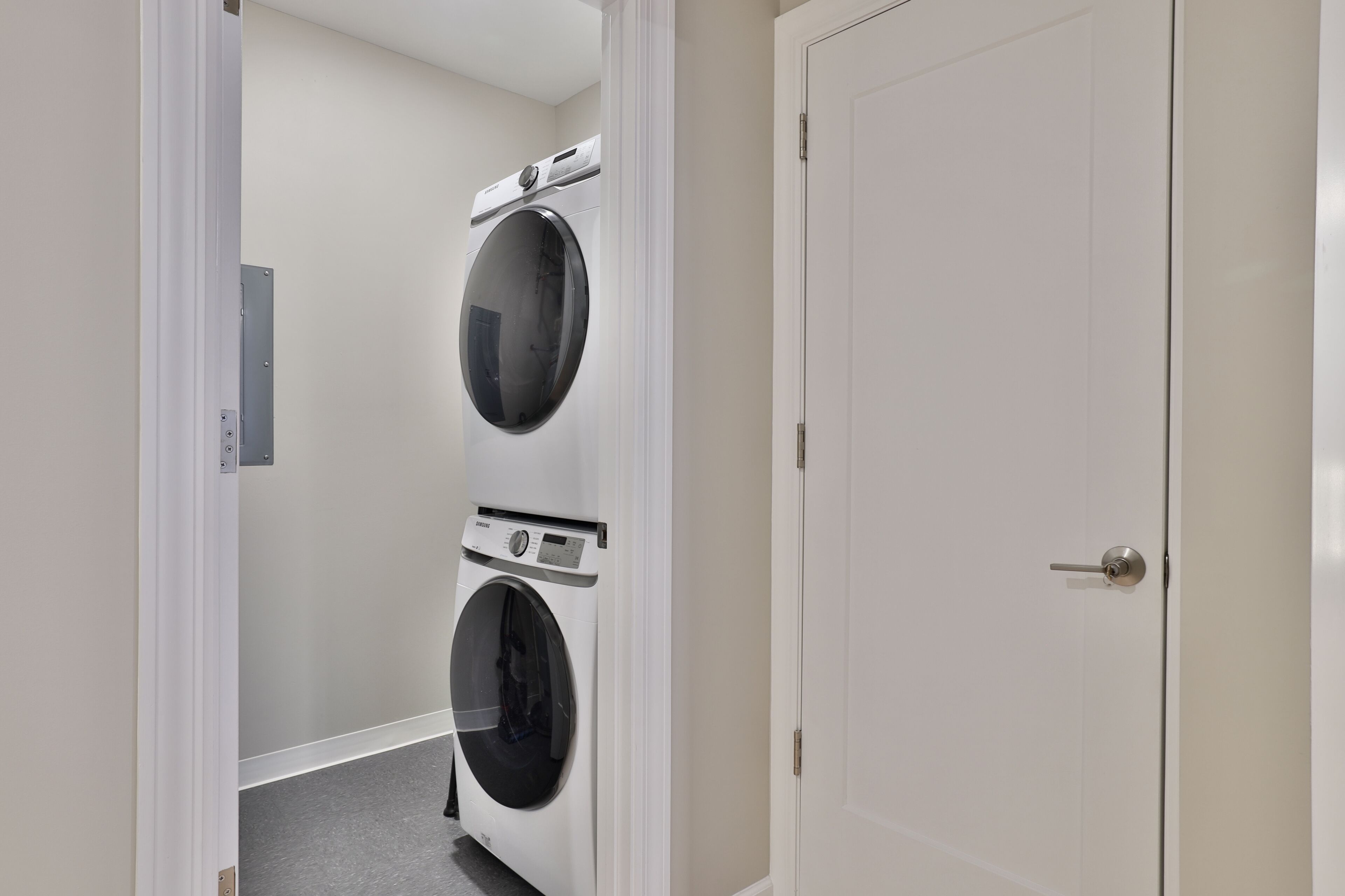 A laundry room with two stacked front-loading washing machines and a closed door.