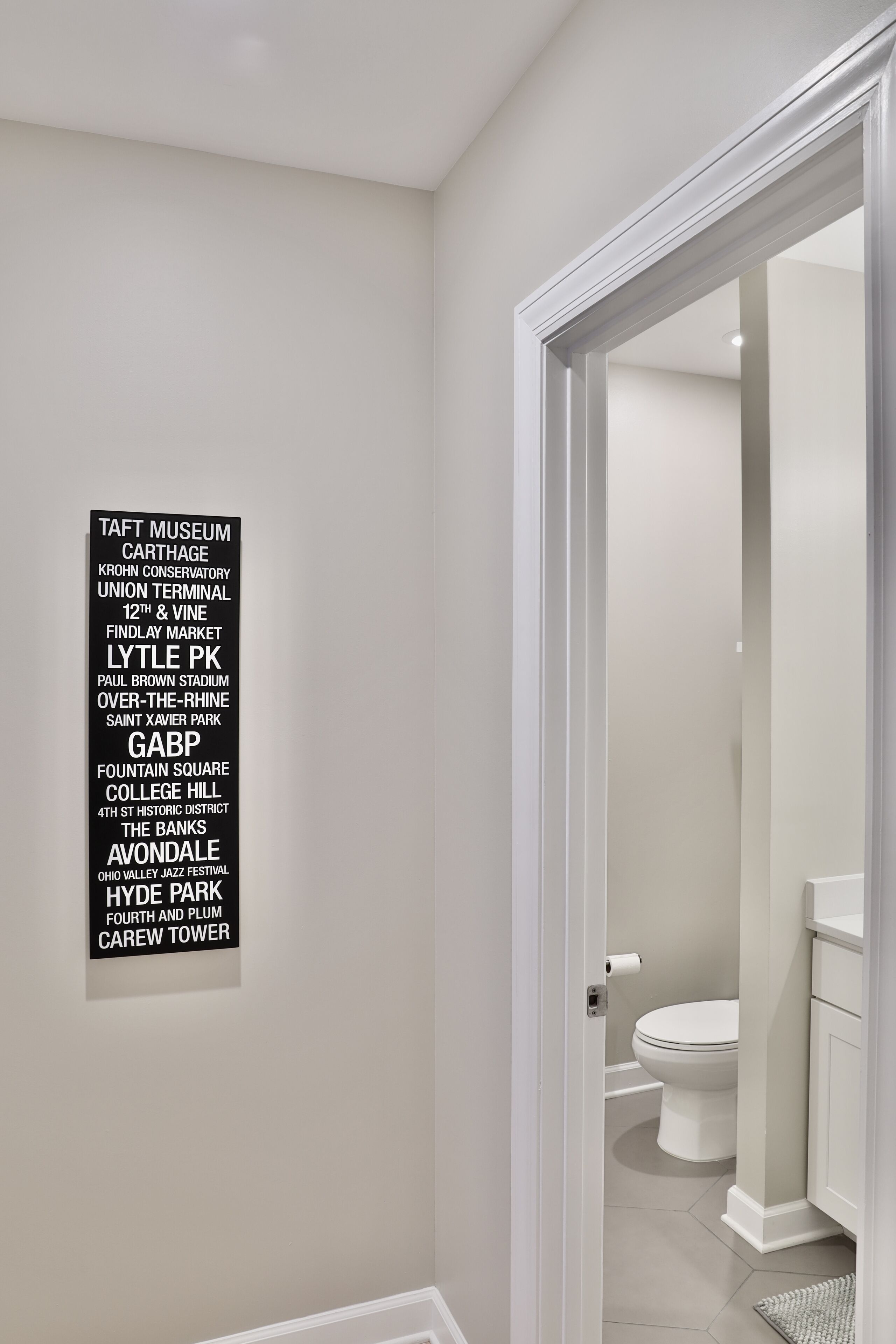 A hallway with a white door leading to a bathroom. A black sign with white text lists various locations and landmarks.