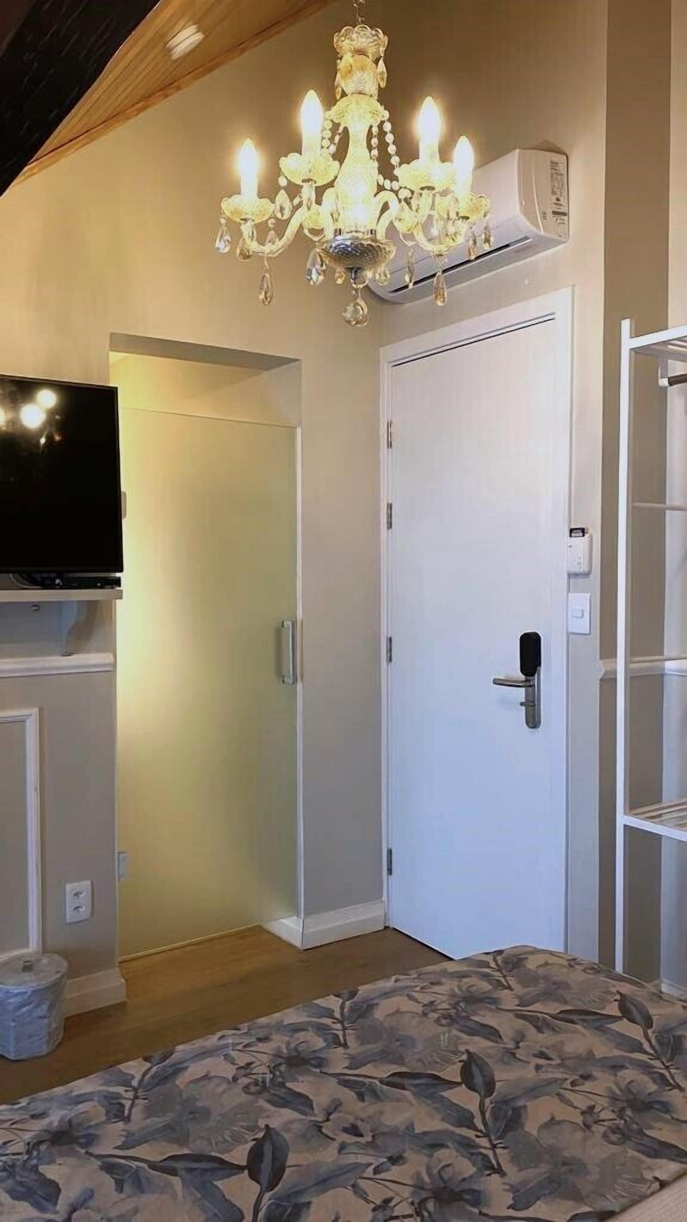 A room with a bed, a chandelier, a television, and a door.