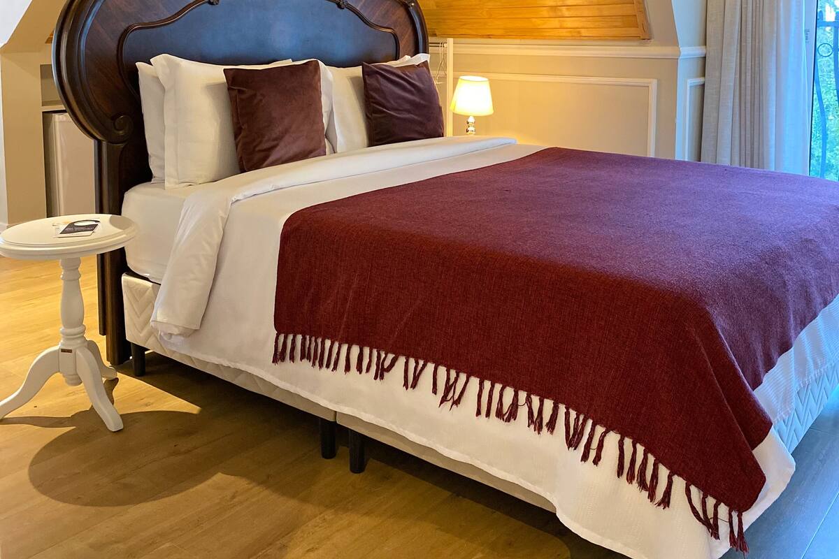 A bedroom with a wooden ceiling, a large bed with a dark headboard, white bedding, and a red throw blanket.