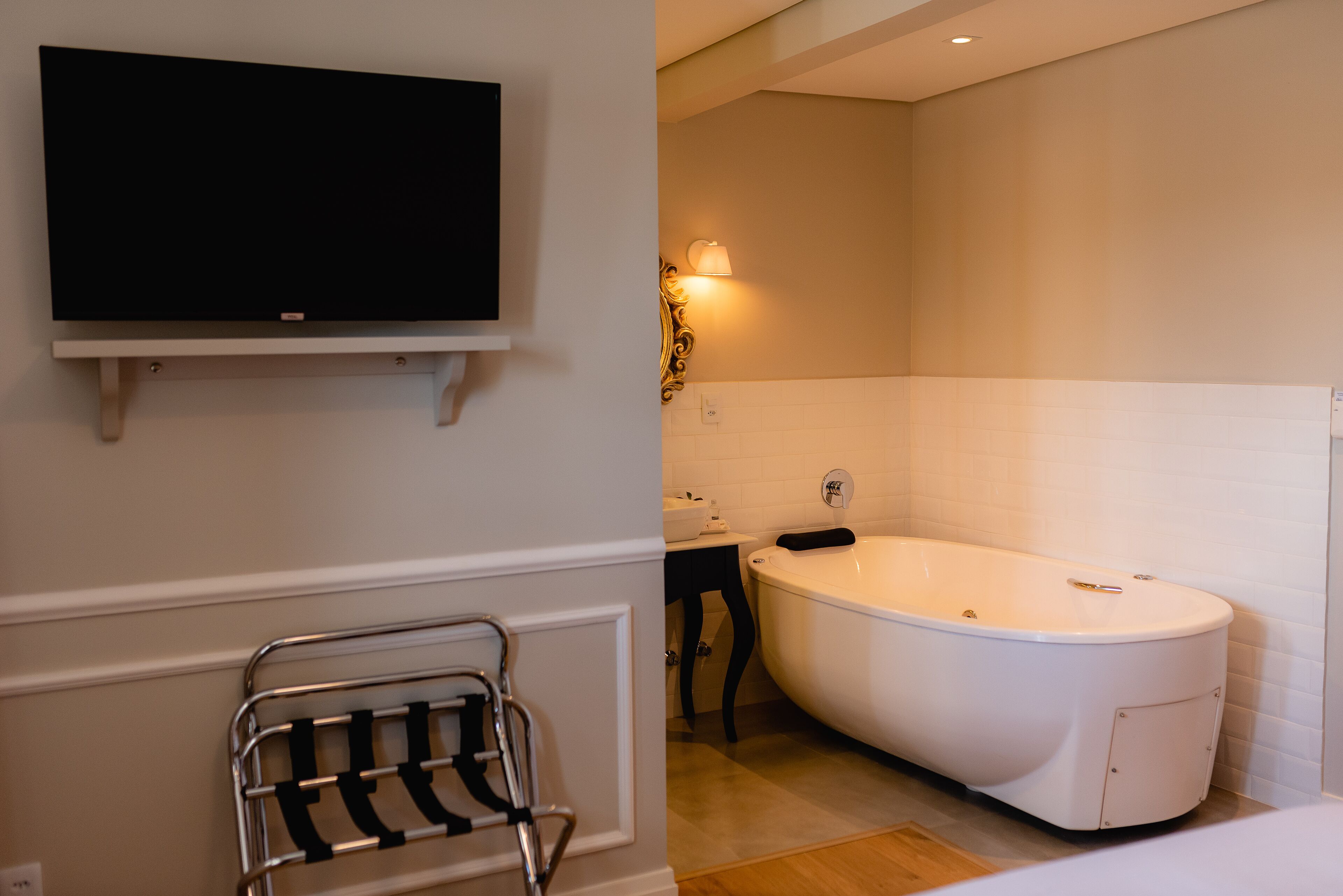 Een moderne badkamer met een vrijstaand bad, een wastafel met spiegel en een wandgemonteerde televisie.
