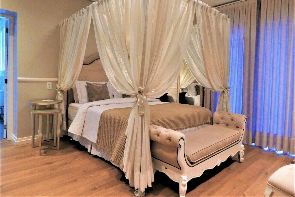A four-poster canopy bed with a tufted headboard, a bedside table, and a nightstand.