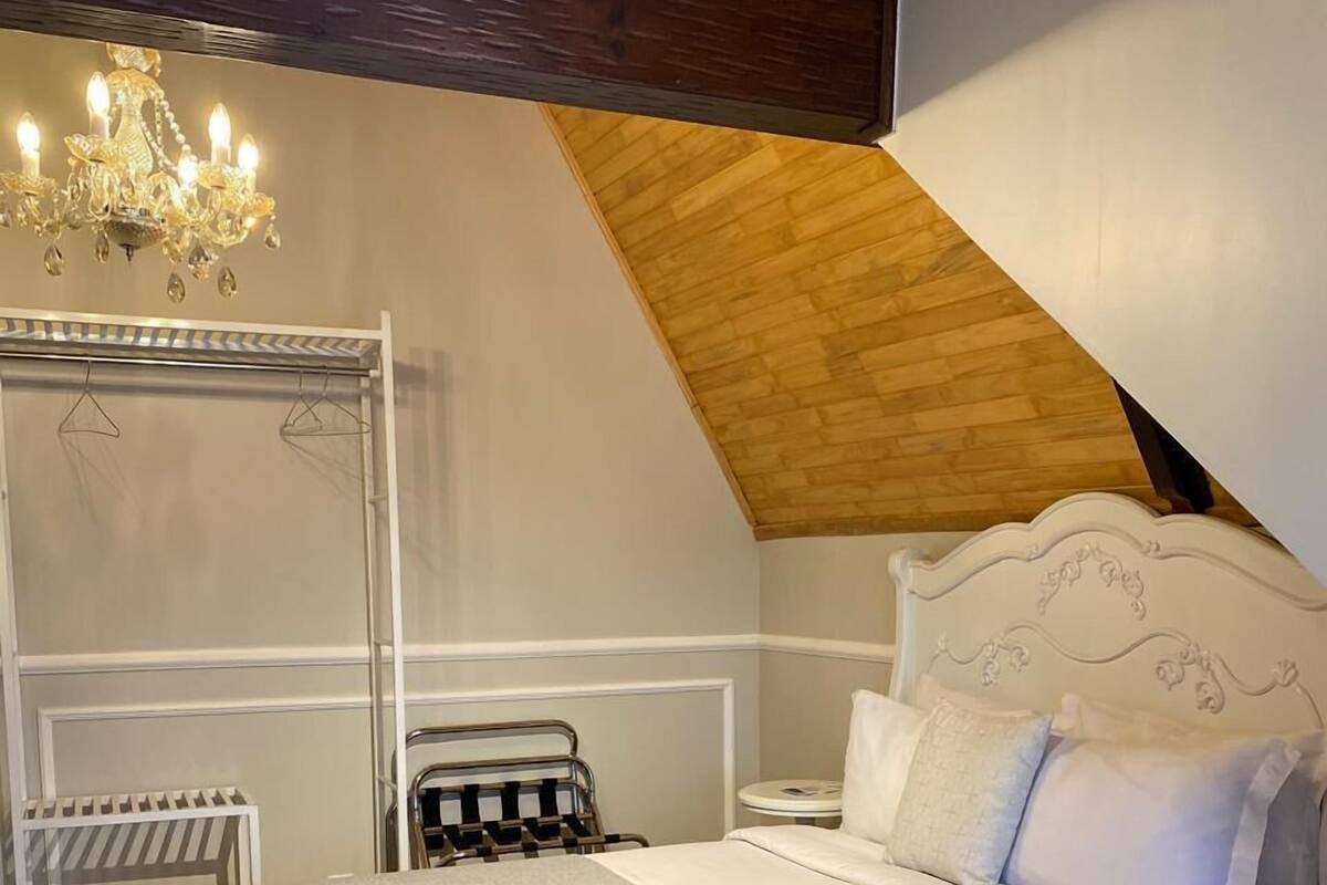 A bedroom with a large bed, a chandelier, a wooden ceiling, and a white headboard.