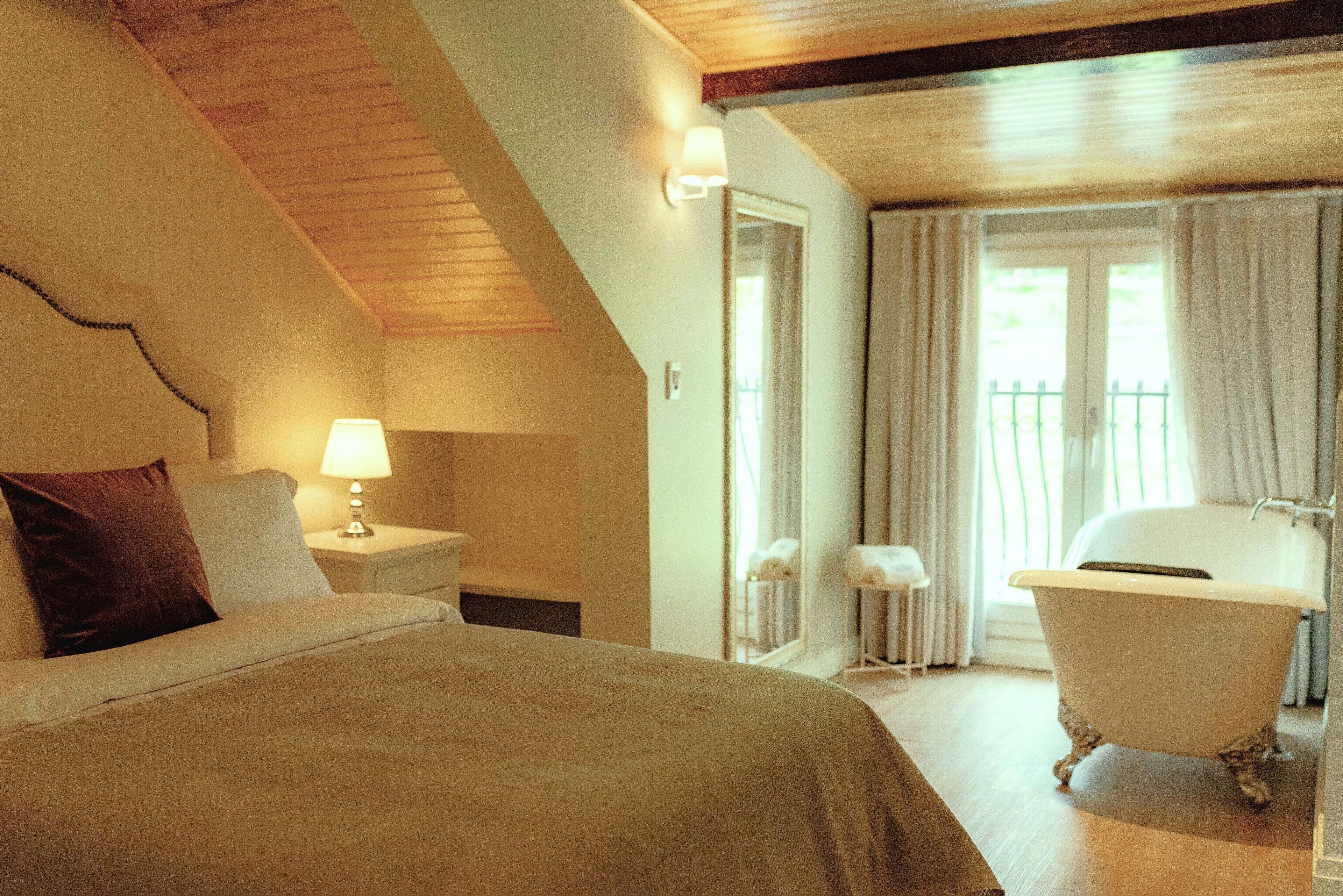 A bedroom with a bed, nightstand, lamp, and a bathroom with a bathtub.