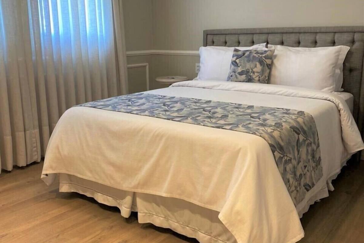 A neatly made bed with a floral bedspread, a grey upholstered headboard, and a white pillow.
