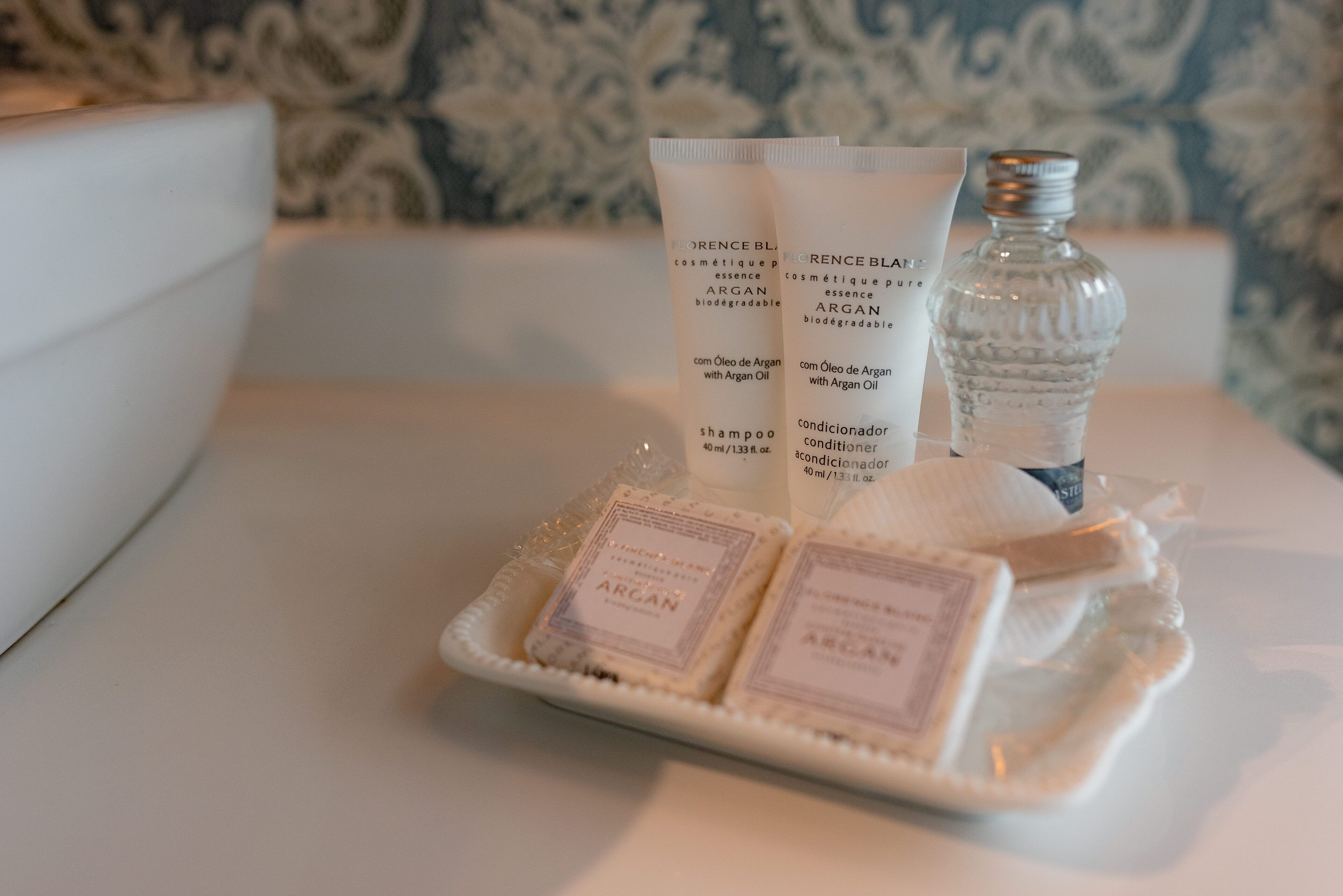 A tray with two bottles of argan oil-based shampoo and conditioner, a small bottle of water, and two bars of soap on a white surface.