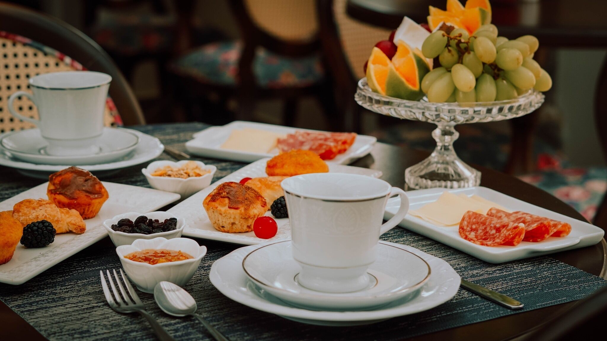 A breakfast setting with pastries, fruits, and cheese on plates, and a cup of coffee.