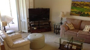 Una sala de estar con sofá, reposapiés, mesa de centro, televisor y un cuadro en la pared.