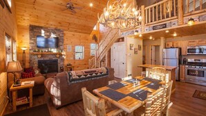 A cozy log cabin interior with a fireplace, a television, a dining area, and a kitchen. - Beautiful ADK Getaway! Trail 4 and Lake Access!  Weekly Discount Available (Old Forge)