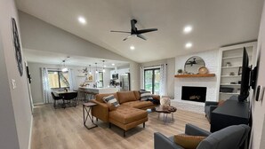 A modern living room with a sofa, armchairs, and a fireplace. There is a kitchen in the background with a dining area. - Great location! All New Super Private Modern Freshly Remodeled Retreat! (Cedar Park)