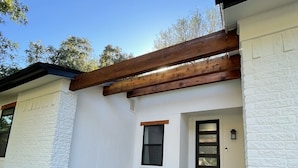 A modern house with a white exterior, a wooden pergola over the entrance, and a small garden with rocks and plants. - Great location! All New Super Private Modern Freshly Remodeled Retreat! (Cedar Park)