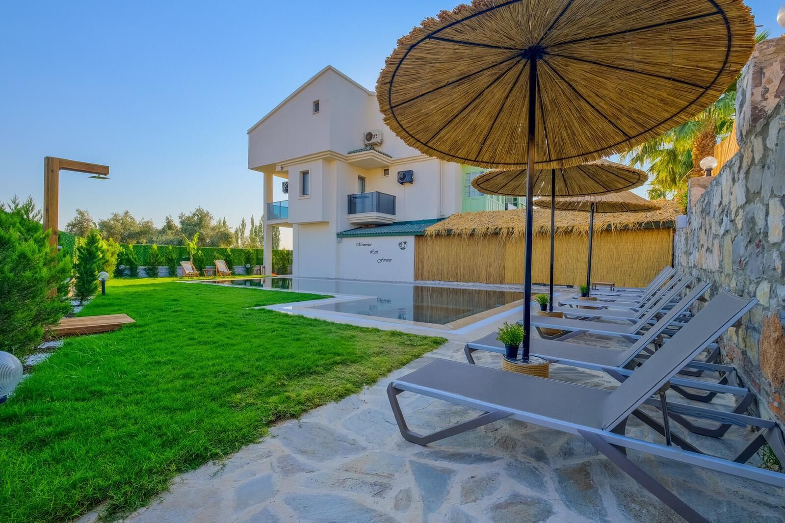 A poolside area with lounge chairs, a stone wall, and a building with a white facade.