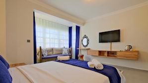 A hotel room with a bed, a TV, a sofa, and a window with curtains.