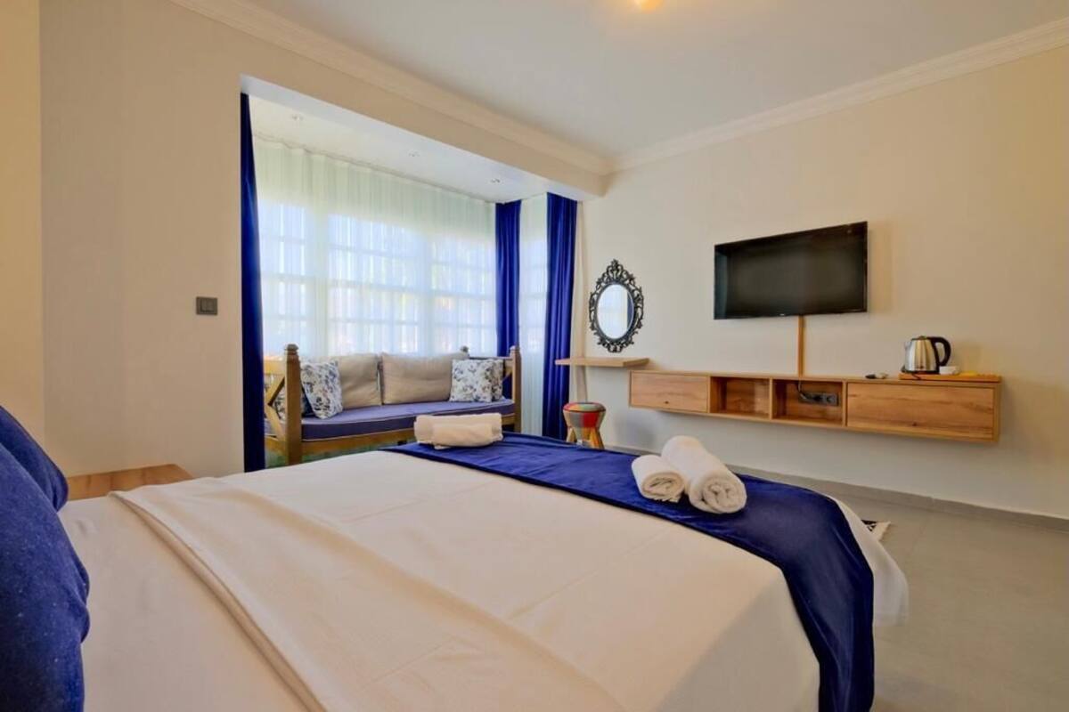 Quarto de hotel com cama, televisão, sofá e janela com cortinas.