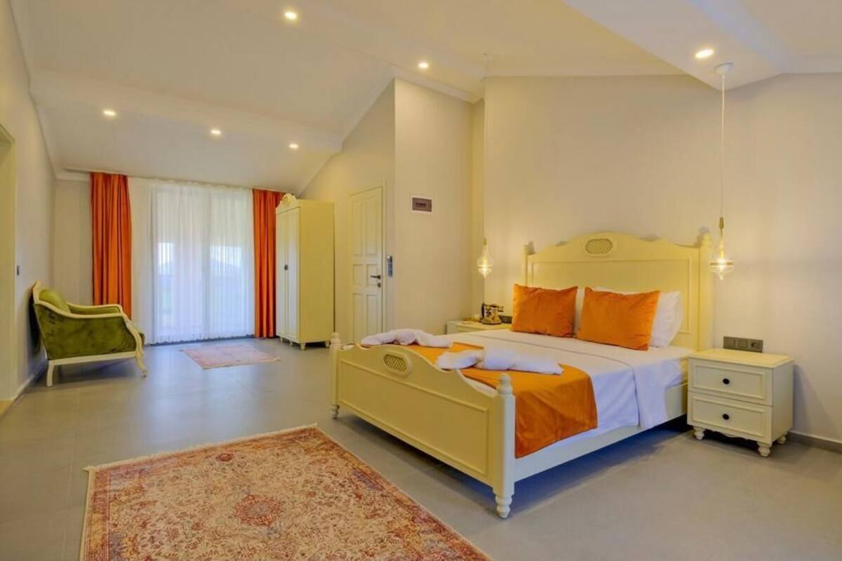 Quarto com cama, mesas de cabeceira, uma cadeira e uma porta.