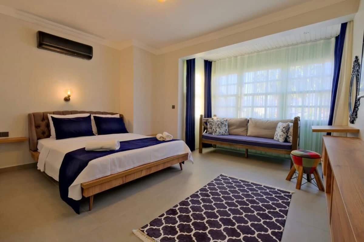 Quarto com cama, sofá, mesinha e janela com cortinas.