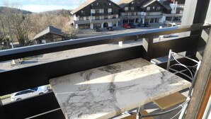 A balcony with a marble table and metal chairs, overlooking a parking area and buildings.