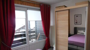 A bedroom with a bed, a wardrobe, a window with curtains, and a radiator.